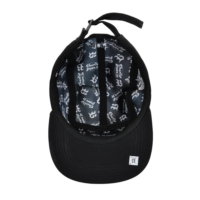 Interior de boné five panel preto, estampa interna com “Charlie Brown Jr.” repetido em branco e ajuste em fivela.